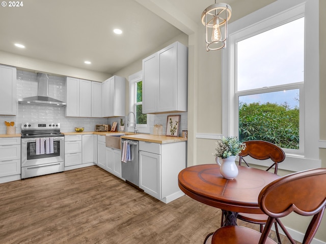 kitchen featuring white cabinetry, stainless steel appliances, wall chimney exhaust hood, light hardwood / wood-style flooring, and decorative light fixtures