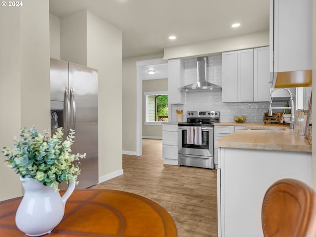 kitchen featuring appliances with stainless steel finishes, white cabinetry, wall chimney range hood, and sink