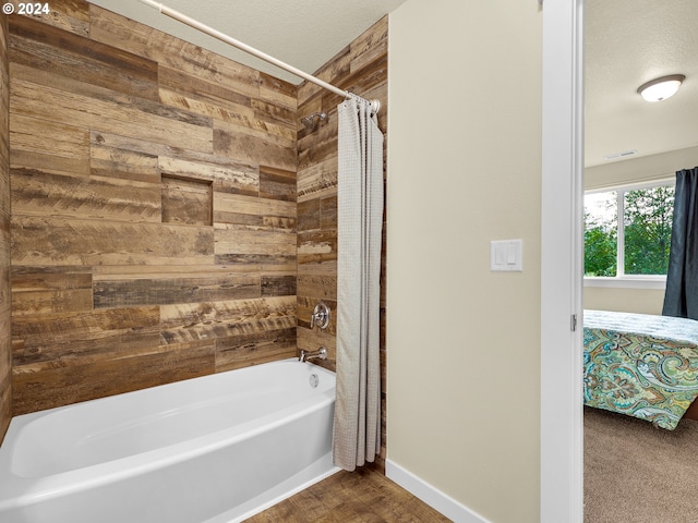 bathroom with a textured ceiling, wood walls, and shower / bath combo with shower curtain