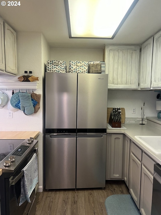 kitchen featuring stainless steel fridge, black range with electric stovetop, dishwasher, dark hardwood / wood-style floors, and sink