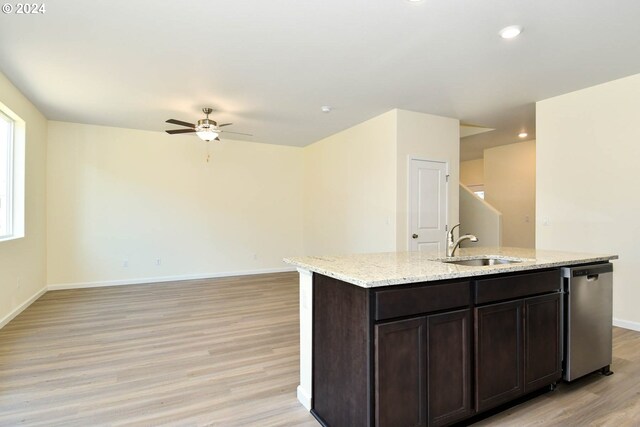 kitchen with baseboards, light wood finished floors, an island with sink, a sink, and stainless steel dishwasher