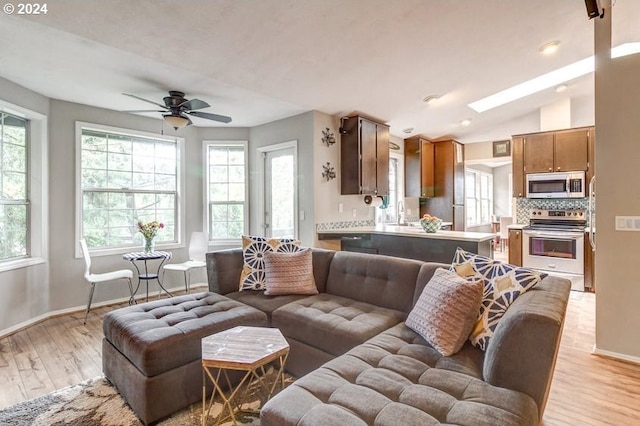 living room with ceiling fan, vaulted ceiling with skylight, a healthy amount of sunlight, and light wood-type flooring