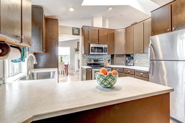 kitchen with kitchen peninsula, appliances with stainless steel finishes, tasteful backsplash, vaulted ceiling, and sink