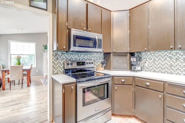 kitchen featuring decorative backsplash, appliances with stainless steel finishes, light hardwood / wood-style floors, and lofted ceiling