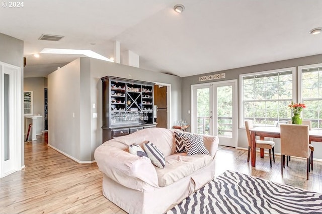 living room with vaulted ceiling, bar, and light hardwood / wood-style flooring