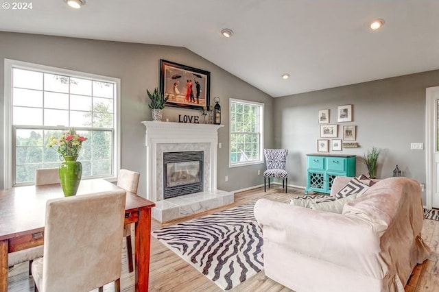 living room featuring a tile fireplace, vaulted ceiling, and light wood-type flooring