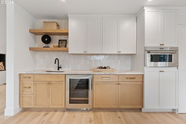 kitchen with light wood-type flooring, beverage cooler, open shelves, a sink, and stainless steel oven