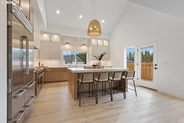 kitchen with premium appliances, light wood-type flooring, high vaulted ceiling, and a center island with sink