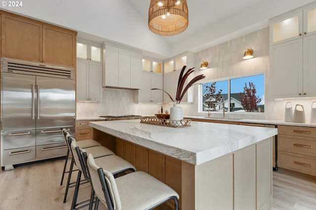 kitchen with vaulted ceiling, built in refrigerator, white cabinets, a kitchen island, and light wood-type flooring