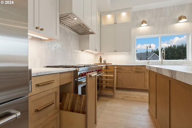 kitchen featuring light wood finished floors, custom range hood, glass insert cabinets, appliances with stainless steel finishes, and backsplash