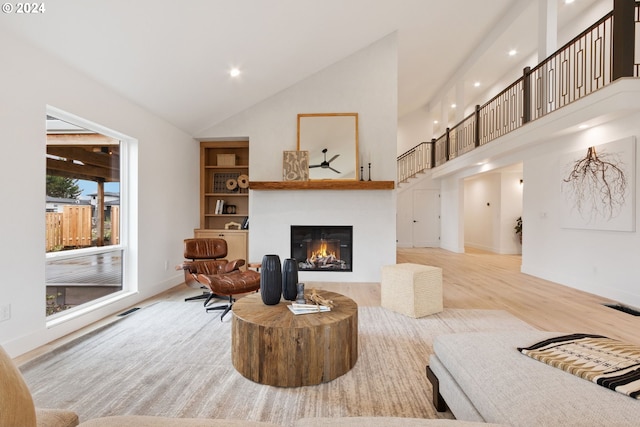 living room featuring light wood-type flooring, high vaulted ceiling, visible vents, and a glass covered fireplace