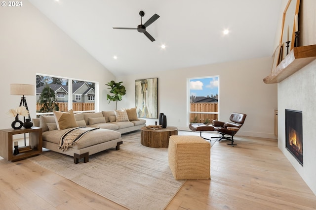 living room with light wood-type flooring, a large fireplace, ceiling fan, and high vaulted ceiling