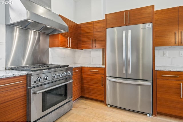 kitchen with appliances with stainless steel finishes, light wood-style floors, backsplash, and wall chimney exhaust hood