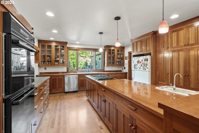 kitchen featuring appliances with stainless steel finishes, sink, light hardwood / wood-style flooring, and decorative light fixtures