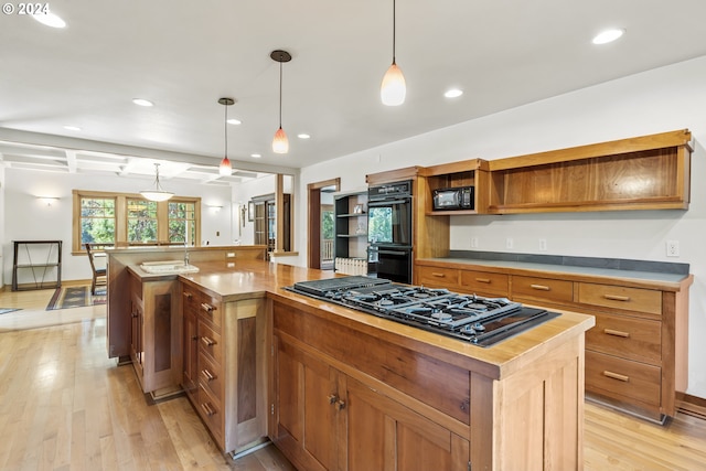 kitchen with light hardwood / wood-style floors, sink, hanging light fixtures, black appliances, and a center island with sink