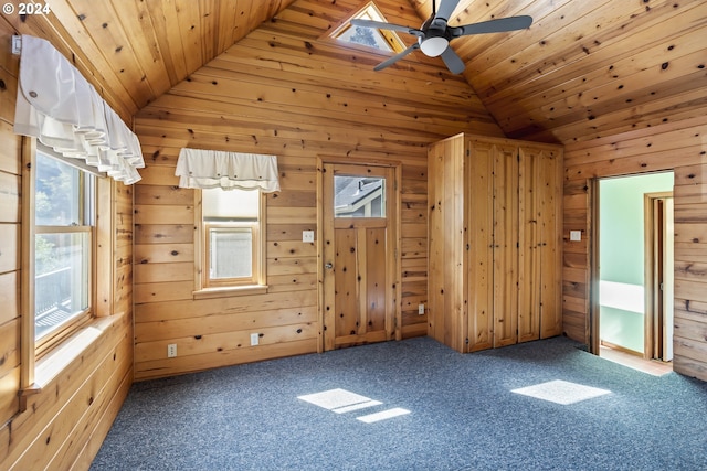 unfurnished room featuring ceiling fan, wooden walls, lofted ceiling with skylight, and wooden ceiling