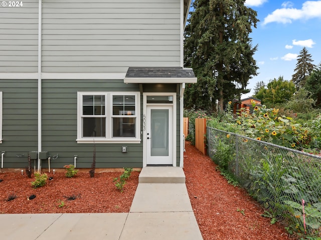 property entrance featuring roof with shingles and fence