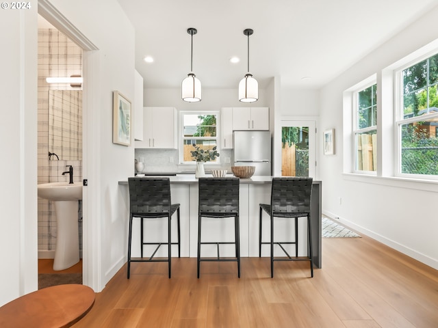 kitchen with stainless steel fridge, light hardwood / wood-style flooring, a breakfast bar area, and white cabinets