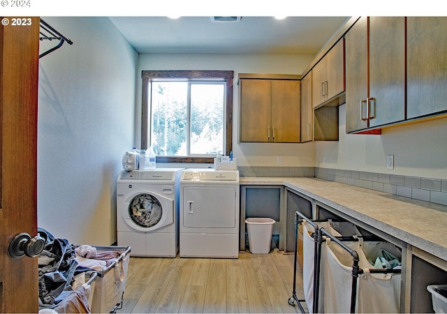 laundry area featuring washing machine and dryer, cabinets, and light hardwood / wood-style floors