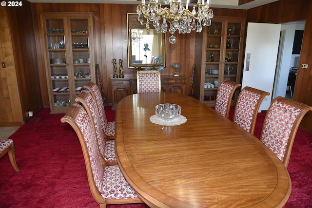 dining space with carpet floors, wooden walls, and a chandelier