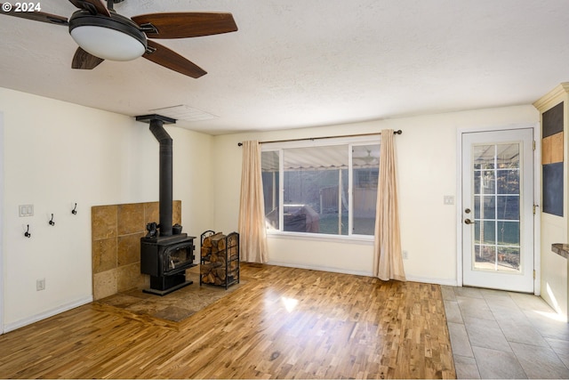 living room with wood-type flooring, a textured ceiling, a wood stove, and ceiling fan