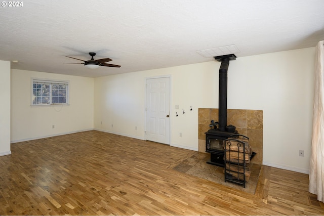 unfurnished living room featuring a textured ceiling, light hardwood / wood-style floors, a wood stove, and ceiling fan