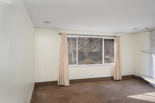 unfurnished room with a textured ceiling and dark carpet