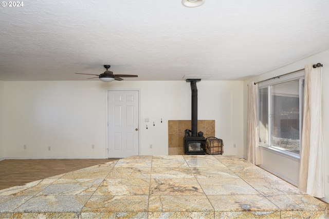 unfurnished living room featuring hardwood / wood-style floors, ceiling fan, a wood stove, and a textured ceiling