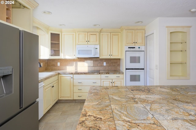 kitchen with backsplash, sink, white appliances, and cream cabinetry