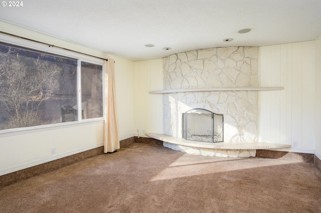 unfurnished living room featuring carpet flooring and a stone fireplace