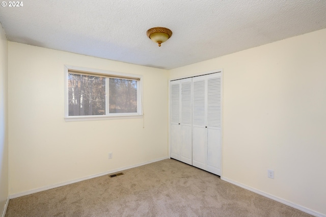 unfurnished bedroom with a textured ceiling, light colored carpet, and a closet