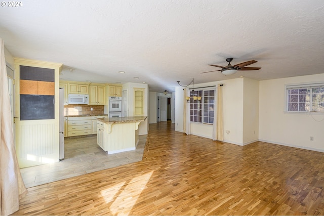 kitchen featuring tasteful backsplash, a breakfast bar, white appliances, a center island, and light hardwood / wood-style floors