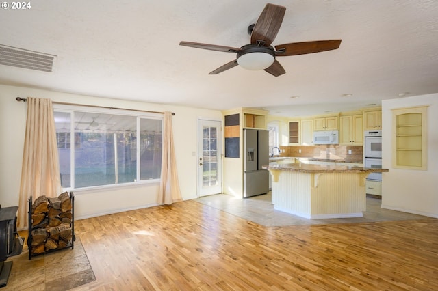 kitchen featuring a center island, light hardwood / wood-style flooring, backsplash, white appliances, and a breakfast bar area