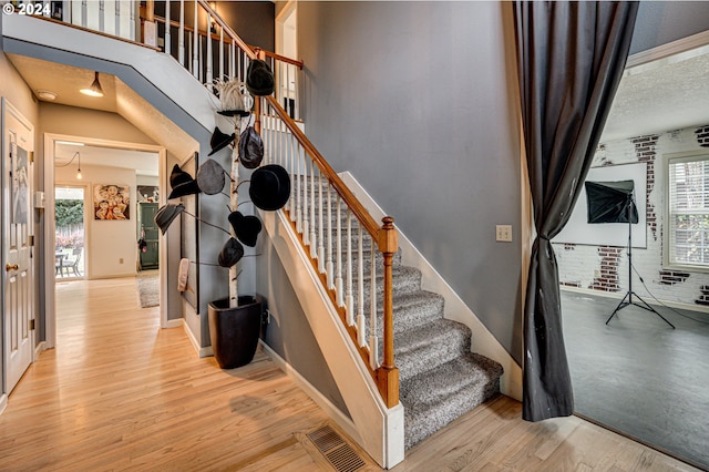 stairs with plenty of natural light, brick wall, and hardwood / wood-style flooring