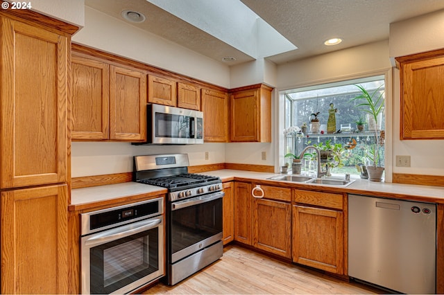 kitchen featuring light wood-type flooring, a skylight, a textured ceiling, stainless steel appliances, and sink