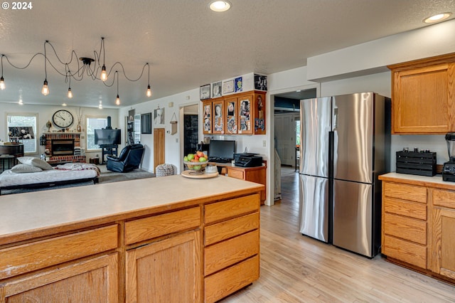 kitchen with stainless steel refrigerator, a fireplace, light hardwood / wood-style floors, and a textured ceiling