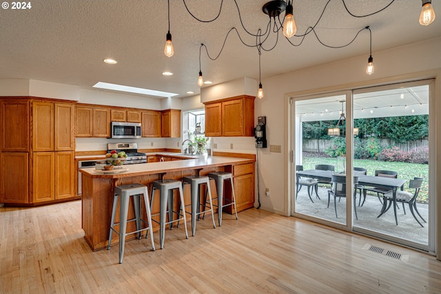 kitchen with light hardwood / wood-style flooring, pendant lighting, a textured ceiling, and appliances with stainless steel finishes