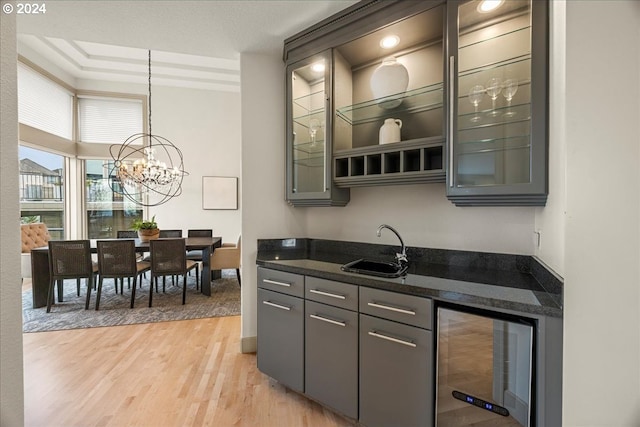 kitchen with sink, light wood-type flooring, decorative light fixtures, beverage cooler, and a chandelier