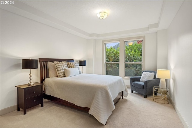 bedroom with a raised ceiling and light colored carpet