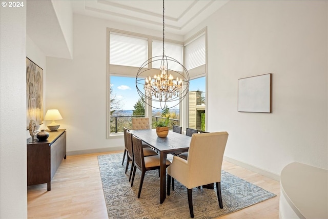 dining space with a raised ceiling, light hardwood / wood-style flooring, and an inviting chandelier