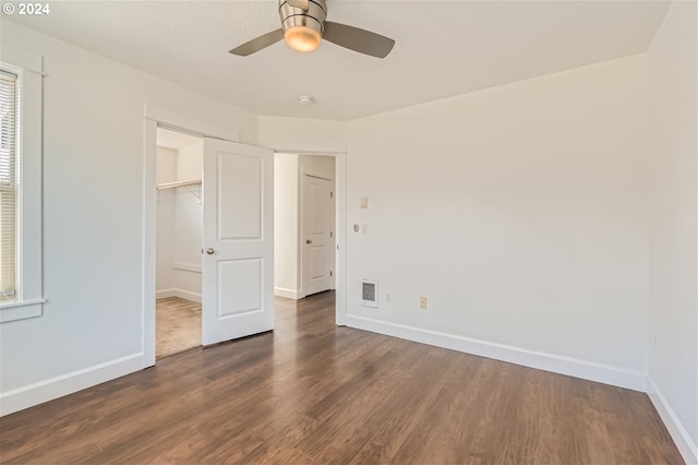 unfurnished bedroom with ceiling fan, a walk in closet, dark wood-type flooring, and a closet