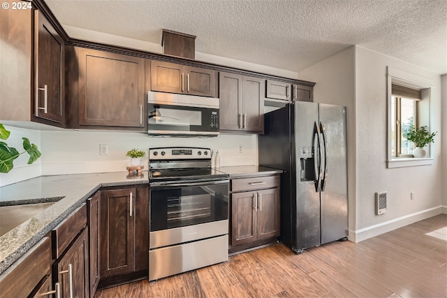 kitchen with refrigerator with ice dispenser, stainless steel electric range, dark brown cabinets, and stone counters