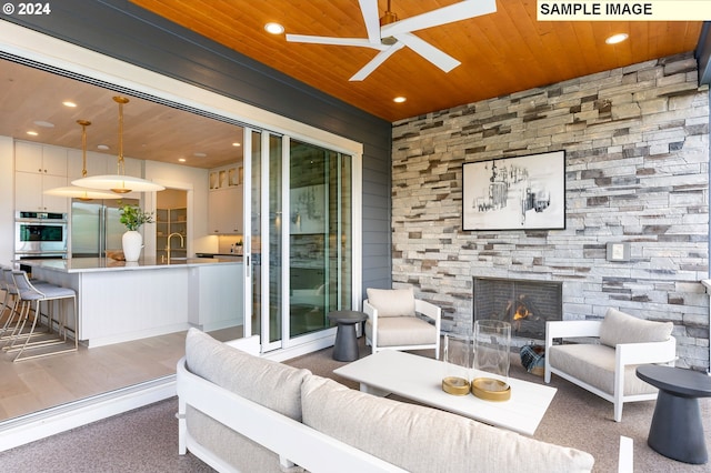 living room featuring ceiling fan, sink, wooden ceiling, a stone fireplace, and dark hardwood / wood-style floors