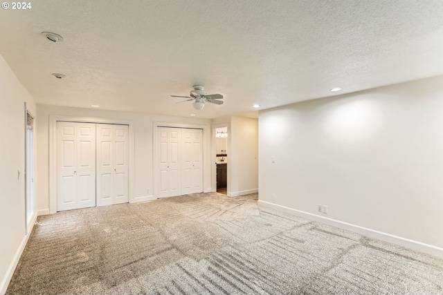 unfurnished bedroom featuring carpet, ceiling fan, a textured ceiling, and multiple closets