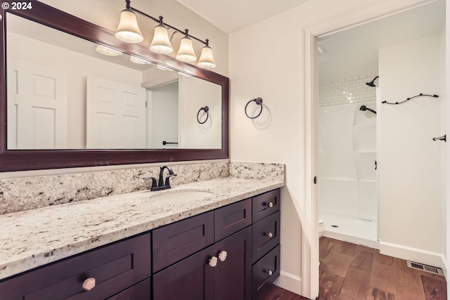 bathroom with a tile shower, hardwood / wood-style flooring, vanity, and toilet