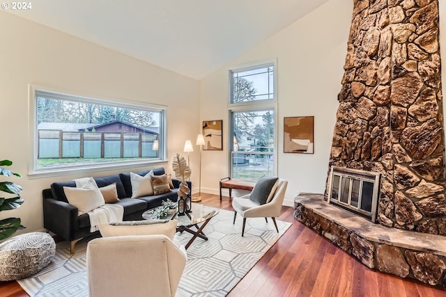 living room with hardwood / wood-style flooring, a stone fireplace, and lofted ceiling