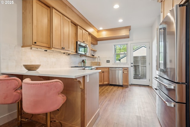 19639 SW Blackbear Ct, Beaverton, OR 97006 - kitchen with stainless steel appliances, a peninsula, light wood-type flooring, a breakfast bar, and recessed lighting