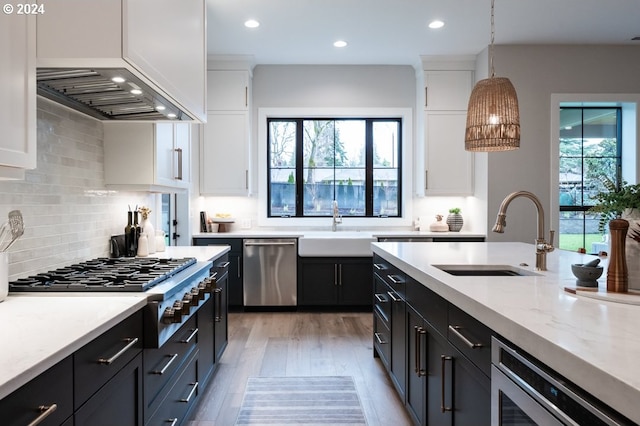 kitchen with pendant lighting, white cabinets, sink, light stone counters, and stainless steel appliances