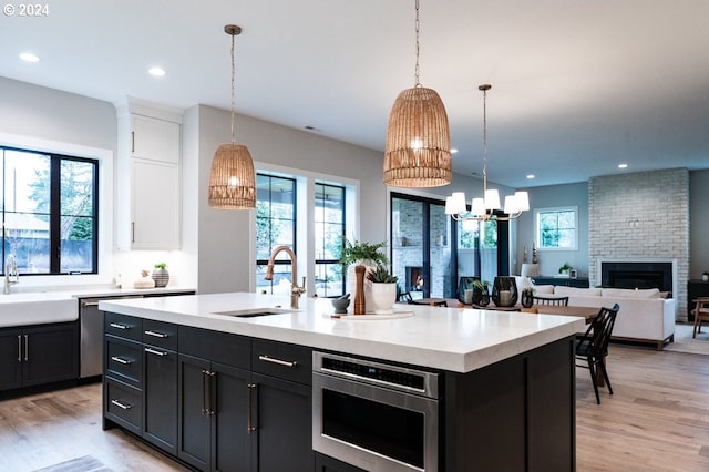 kitchen with sink, an island with sink, decorative light fixtures, and a brick fireplace