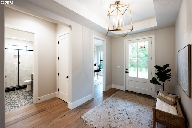 entryway with a notable chandelier, light hardwood / wood-style flooring, and a tray ceiling